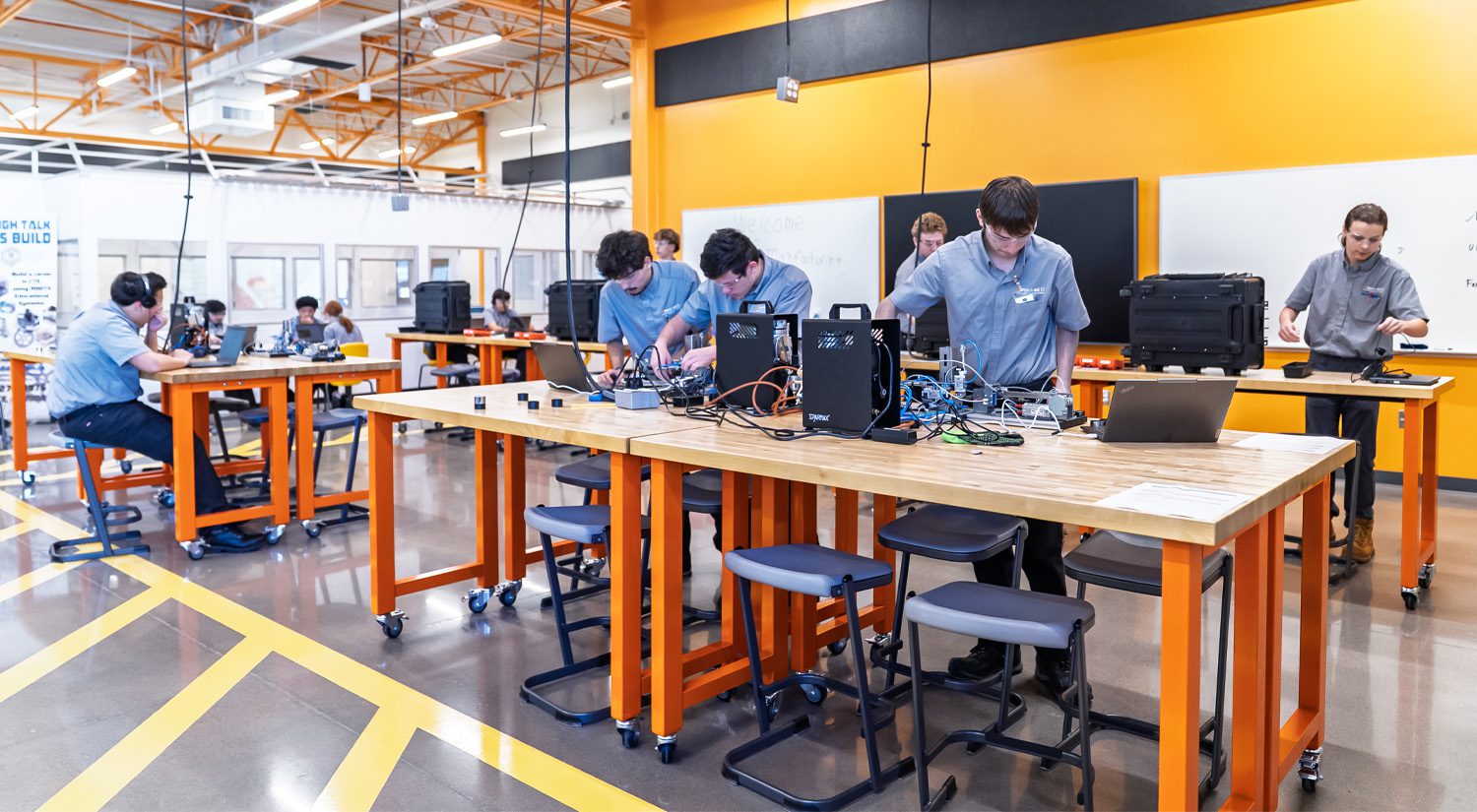 Students in a modern advanced manufacturing lab collaborate at workstations, assembling and testing equipment with tools and laptops in a bright, hands-on CTE learning environment.