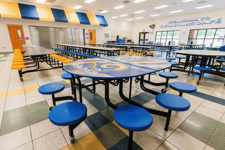 Modern school cafeteria with colorful seating, round tables, and flexible dining furniture in a bright, open space with large windows.