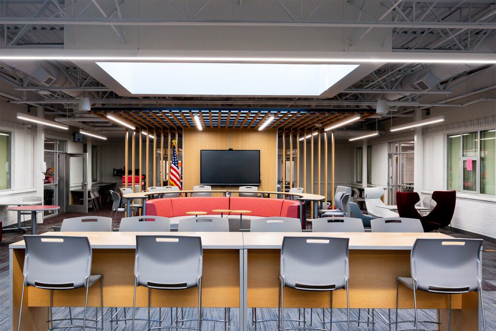 Modern learning commons with tiered seating, large display screen, and flexible furniture for group collaboration.