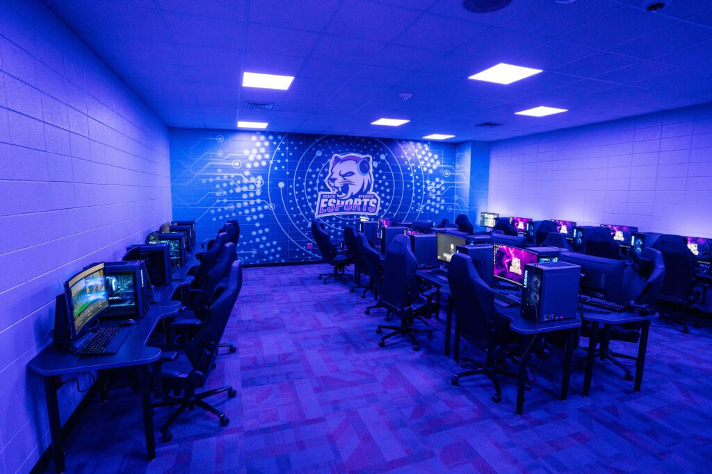 Modern middle school esports lab with gaming PCs, blue lighting, and a team logo on the back wall.