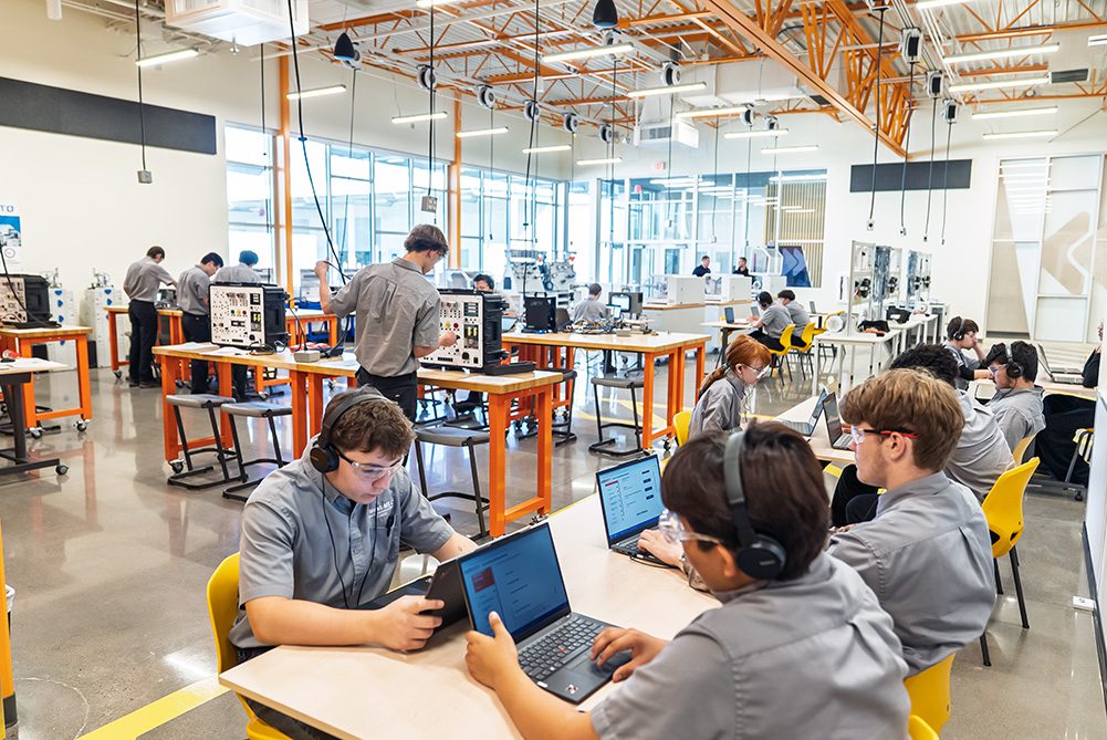 Students work in a modern CTE classroom with laptops and technical equipment.