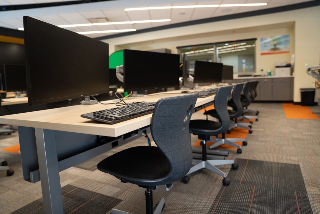 Clean, modern computer lab with large monitors, ergonomic chairs, and collaborative workstation layout.