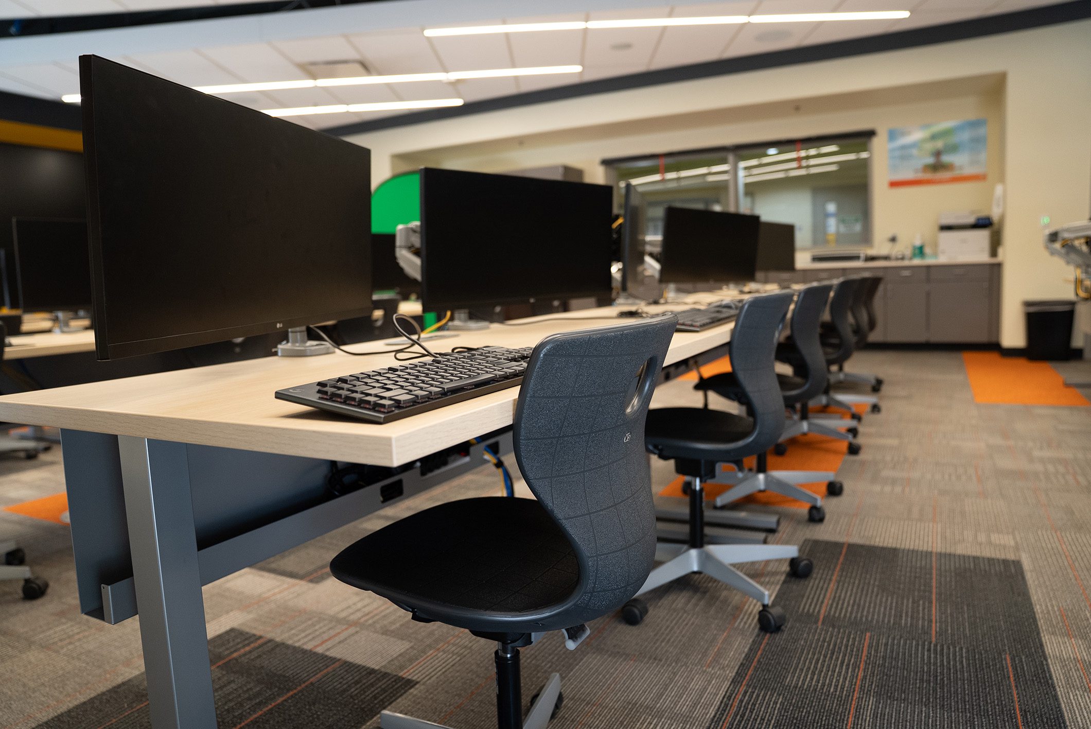 Clean, modern computer lab with large monitors, ergonomic chairs, and collaborative workstation layout.