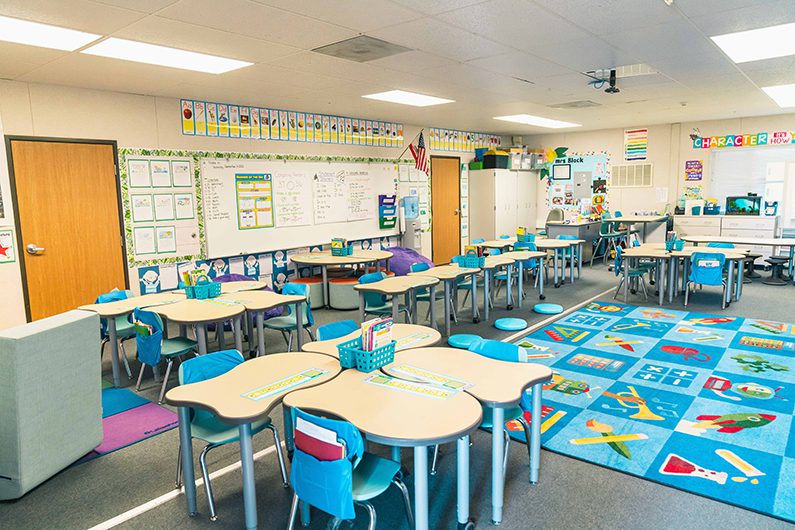 Elementary classroom with colorful furniture, flexible desks, learning rugs, and student work displayed on walls.