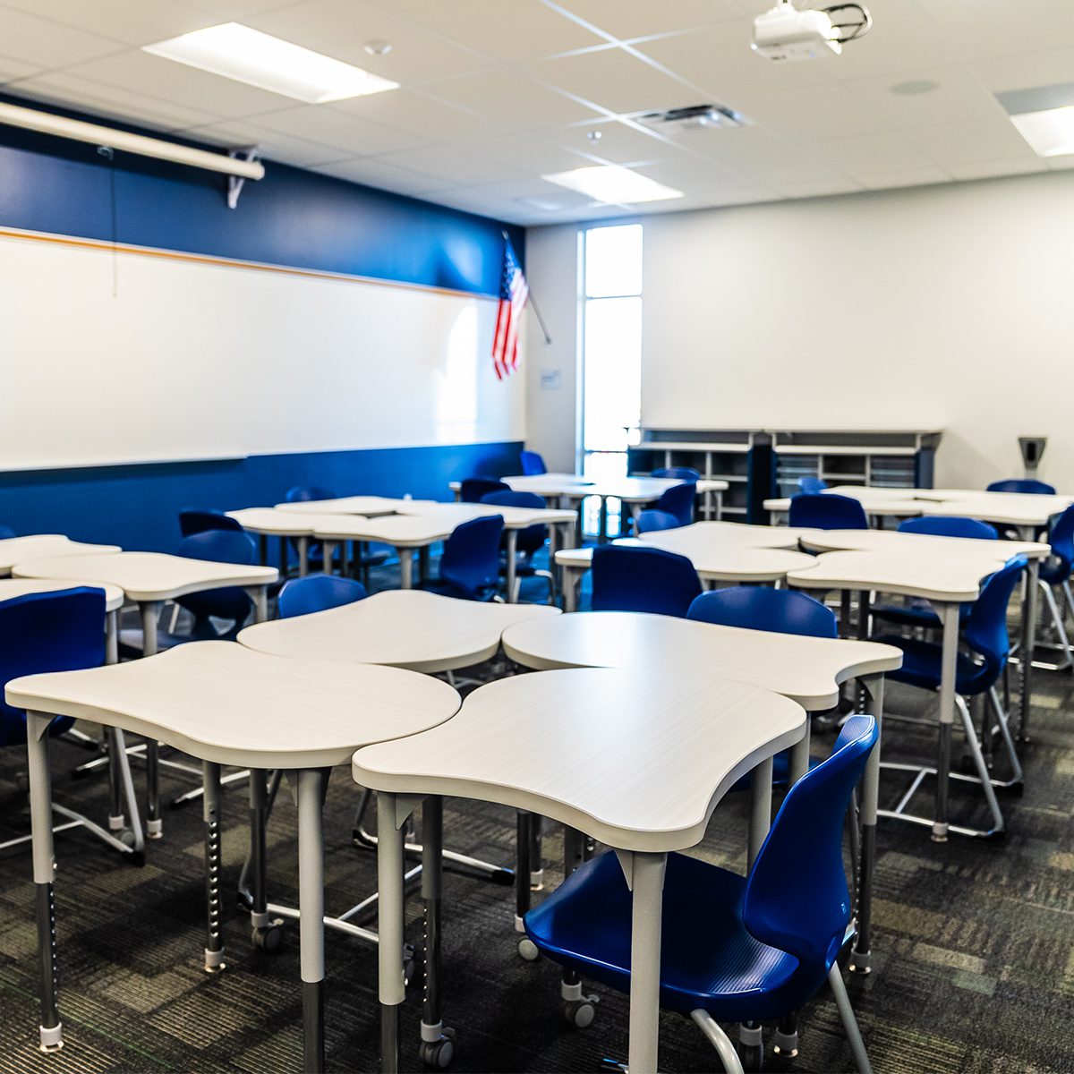 Modern classroom with flexible modular student desks and blue chairs arranged for collaborative learning, featuring a whiteboard and projector at the front.