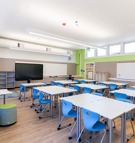 Modern classroom with flexible student desks, blue chairs, interactive display, and collaborative seating designed to support active learning and classroom engagement.