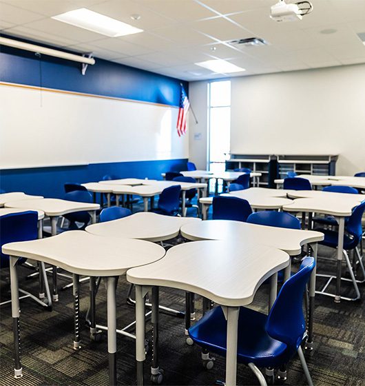 A modernized K-12 classroom featuring collaborative clover-shaped student desks, blue chairs, a whiteboard, and bold navy accent walls in a Goodyear, Arizona school.