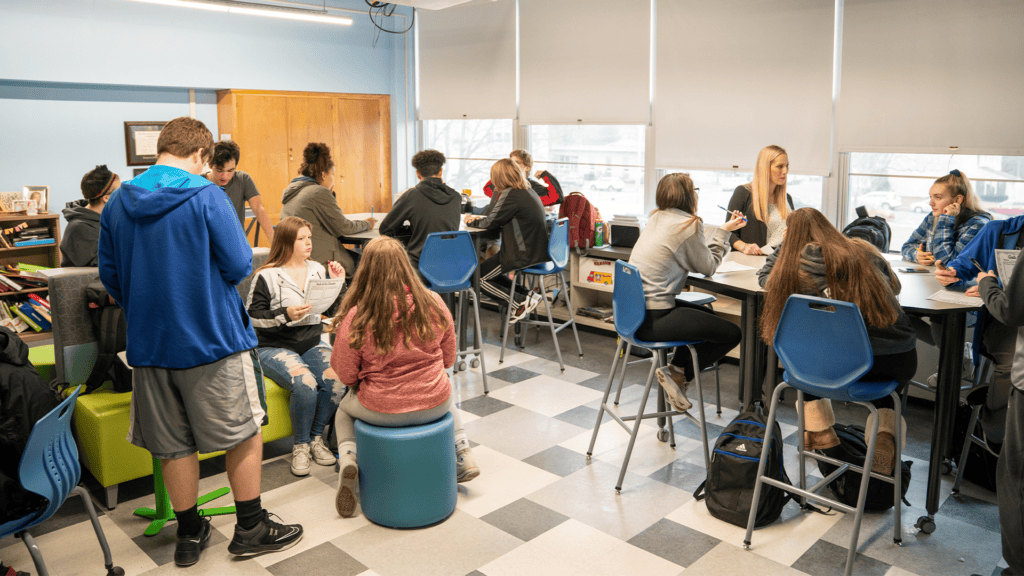 Students collaborate in small groups in a flexible classroom with varied seating while teachers provide support.
